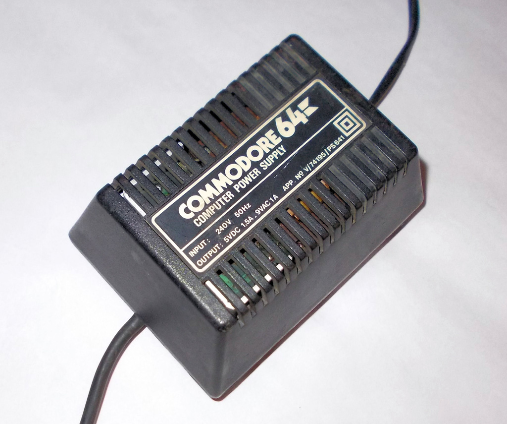 Czarny, masywny zasilacz Commodore 64 w kształcie cegły z naklejką Commodore 64